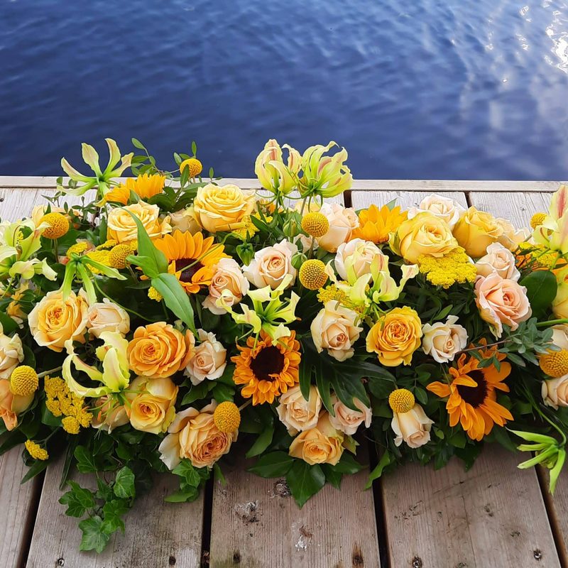 Rouwstuk in geel en oranje met zonnebloemen en rozen, gemaakt door Bloemies