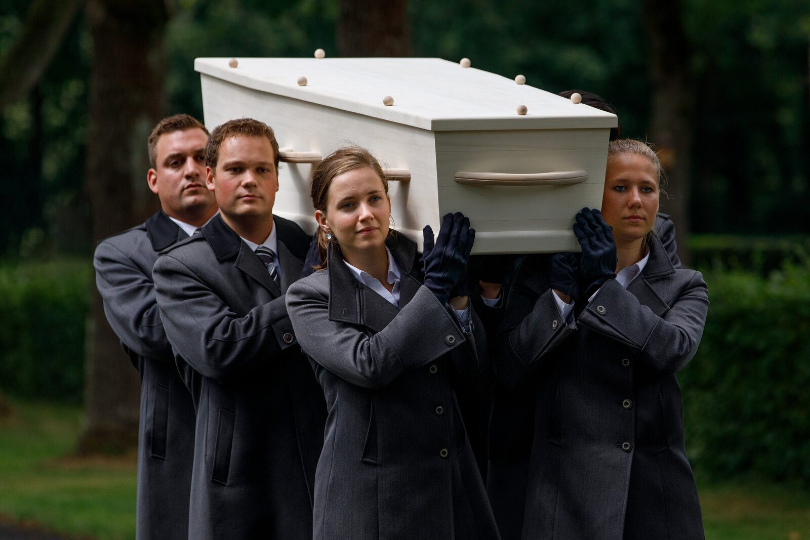 Een gemengd team van dragers draagt een witte kist op de schouders bij een uitvaart