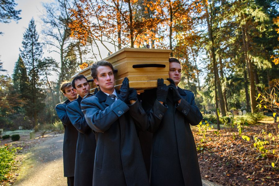 Dragers in donkere overjassen dragen een kist bij een uitvaart