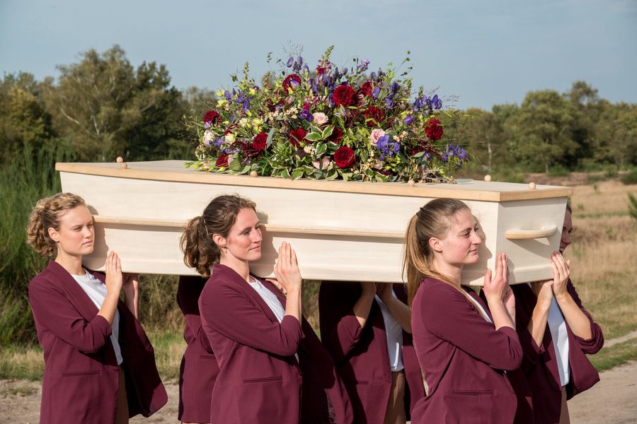 Dragers in bordeauxrode jasjes dragen een kist met bloemen