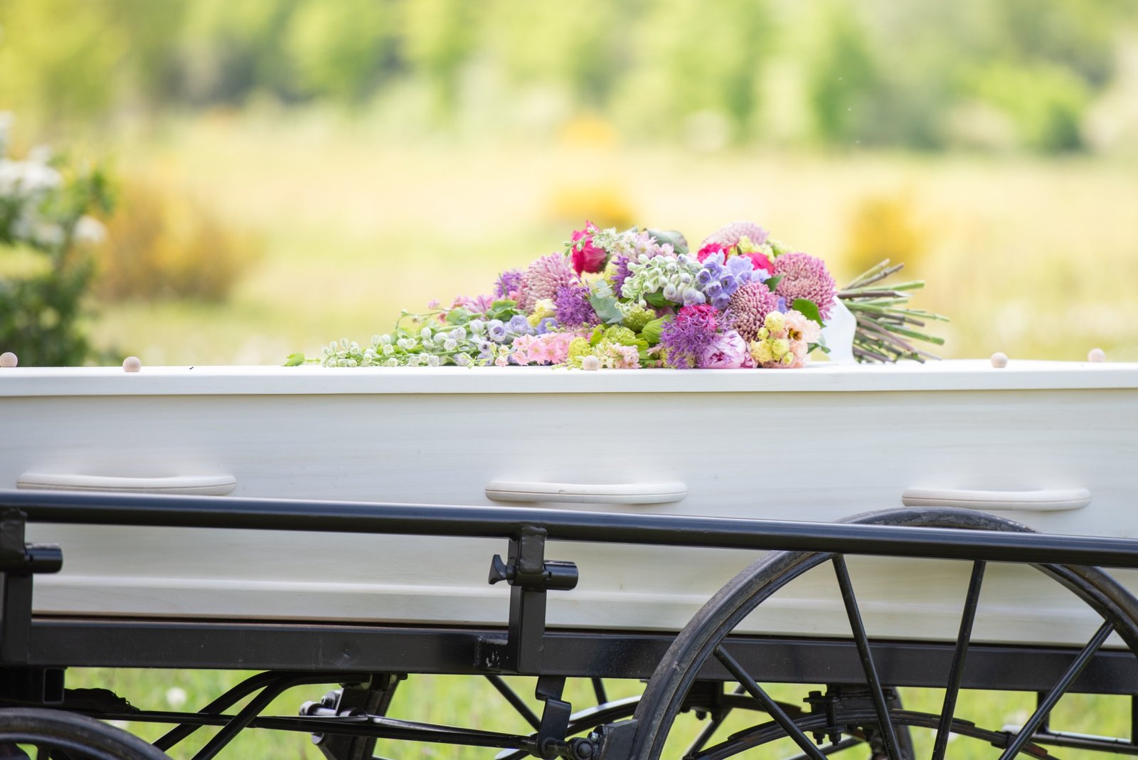 Witte houten kist met een boeket op een baarwagen, buiten in het groen