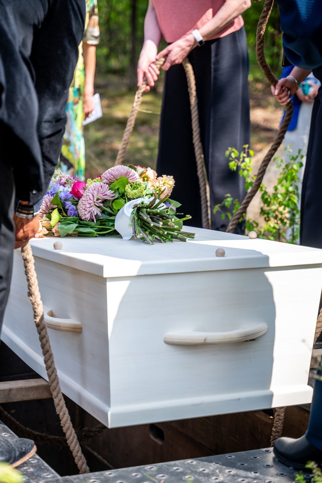 Familie laat een witte houten kist met bloemen met touwen in het graf zakken
